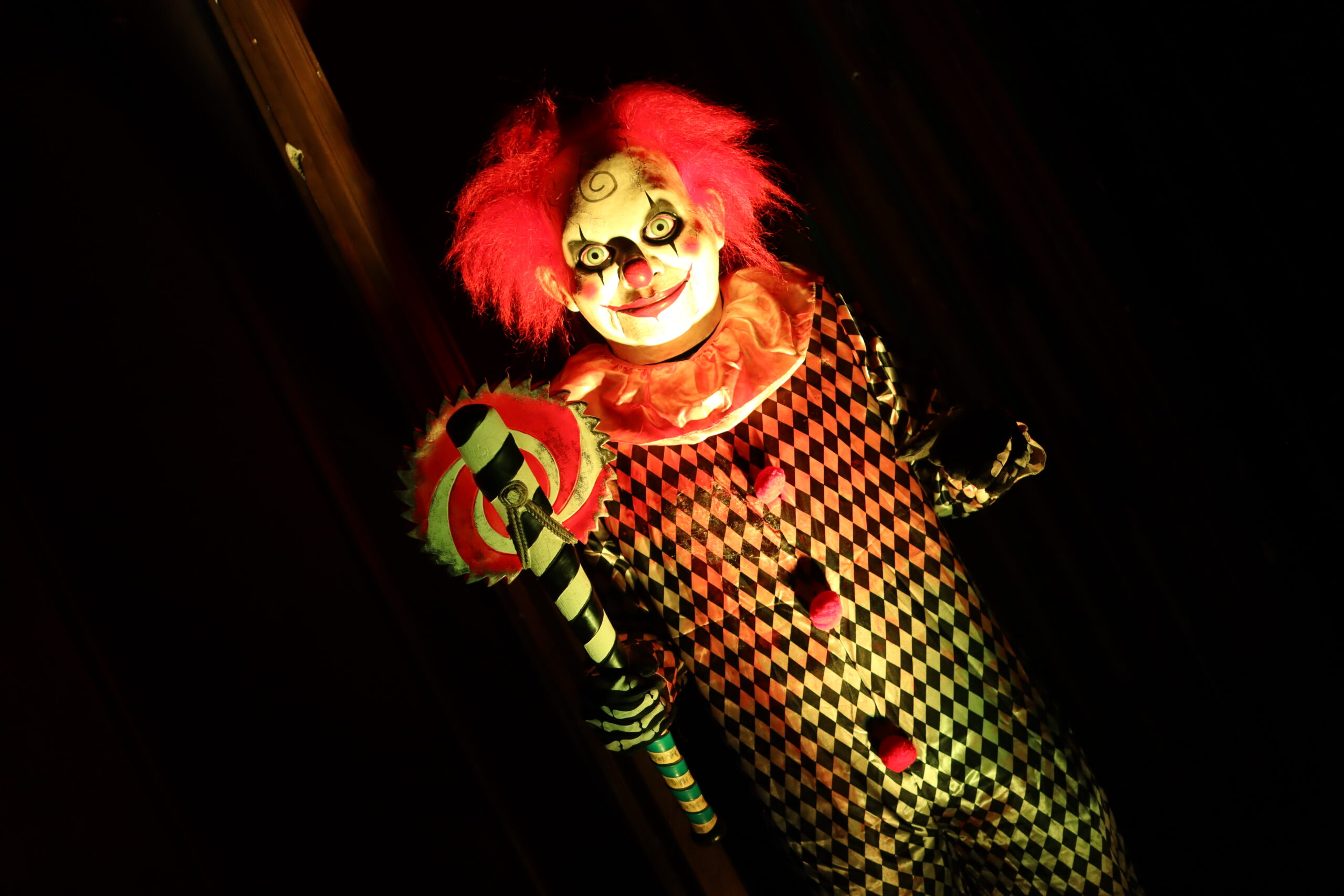 A person dressed as a clown with a red wig holding a circular saw