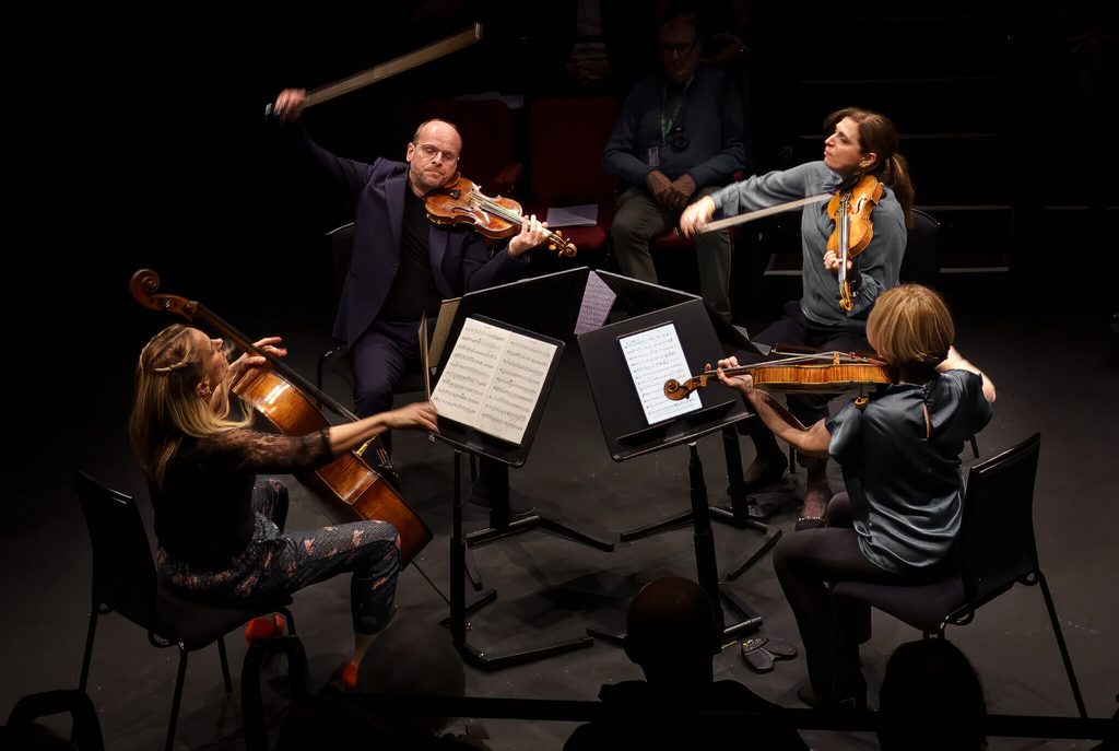 A quartet of 4 classical musicians playing their instruments including violin and cello