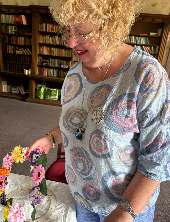 A woman with blonde hair and glasses holding a handmade floral wreath