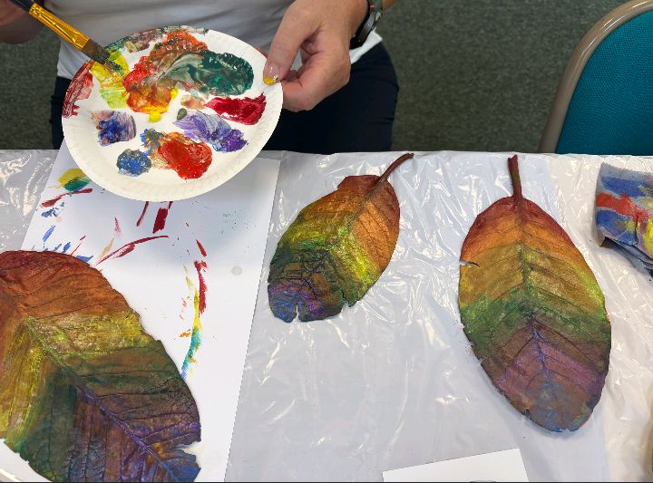 A person with a paint palette painting leaves rainbow coloured for an autumn craft